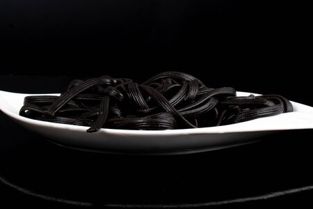 Black tagliatelle (pasta made with cuttlefish ink) on white elegant and simple plate with basil leaf, clean dark black backgroundの写真素材
