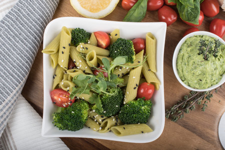 Gluten-free fresh cooked penne pasta from green peas isolated on wooden board. basil, tomato, avocado and coriander in a white bowl. shot from above and closeup. food background italian penneの写真素材