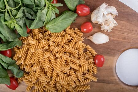 Gluten-free penne pasta from chickpeas, red lentils on wooden cutting board. basil,tomatoes and garlic. shot from above and closeup.food background italian penne and fusilliの写真素材