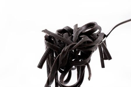 Black fresh cooked tagliatelle pasta on fork isolated (pasta made with cuttlefish ink) with basil leaf, on simple white plate and clean white backgroundの写真素材