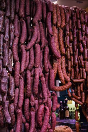 Many homemade German mix of meat specialties, speck ham sausages pile or stack on counter top, for sale, during food festival, outdoor outside marketplace, spicy and tasty fresh specialty for saleの写真素材