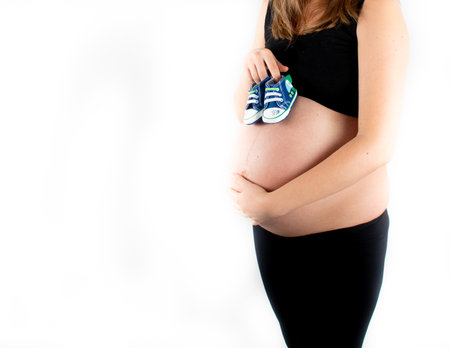 Pregnant woman holding baby boy small shoes in hands, happy pregnancy expecting gift concept. Closeup of mother to be isolated on white backgroundの写真素材