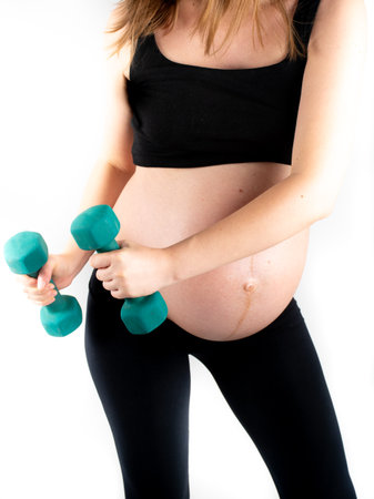 Active healthy pregnant woman exercising with dumbells, isolated on white background. The young expecting mother holding baby in pregnant belly. Maternity prenatal care and woman pregnancy concept.の写真素材