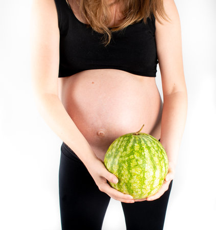 Pregnant woman holding watermelon in her hands. Healthy lifestyle dieting for healthy pregnancy life. Small skinny slim girl posing on white background. Fruit and vegetables vitamins and nutrientsの写真素材