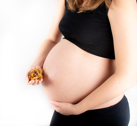 Pregnant woman holding granola or muesli in hands. Healthy eating concept, breakfast idea, diet and nutrient rich food. Small bump belly pregnancy lifestyle. Slim blonde modelの写真素材