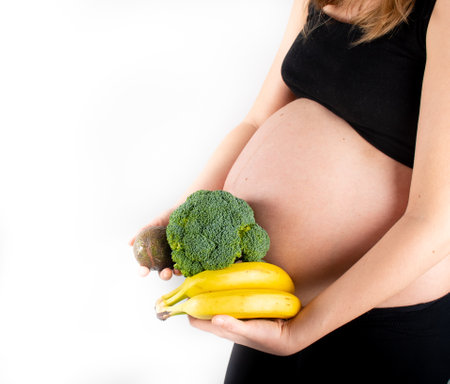 Pregnant woman holding vegetables in hands. Healthy eating concept. Pregnancy, slim skinny girl in black top and leggings isolated on white background. Diet and freshnessの写真素材