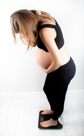 Pregnant woman measures her weight gain in pregnancy on weight scale. Healthy diet eating concept. Slim young skinny fit lady girl model posing on white backgroundの写真素材