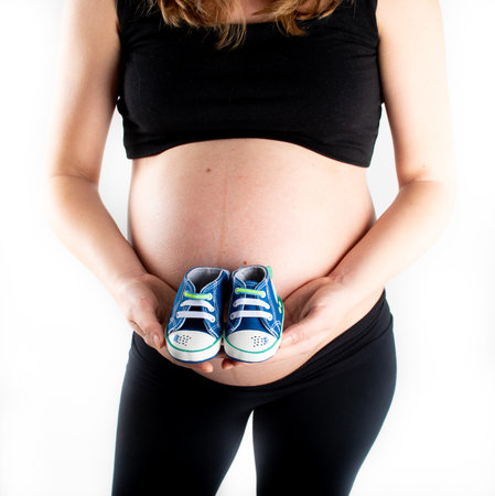 Pregnant woman holding baby boy small shoes in hands, happy pregnancy expecting gift concept. Closeup of mother to be isolated on white backgroundの写真素材