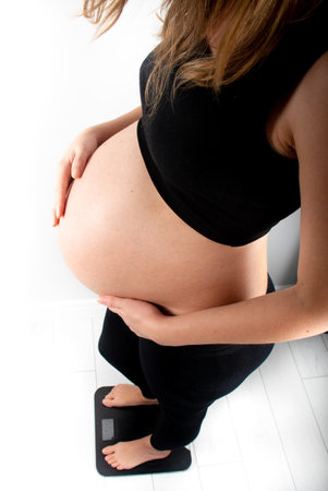Pregnant woman measures her weight gain in pregnancy on weight scale. Healthy diet eating concept. Slim young skinny fit lady girl model posing on white backgroundの写真素材