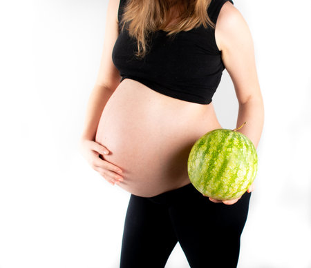 Pregnant woman holding watermelon in her hands. Healthy lifestyle dieting for healthy pregnancy life. Small skinny slim girl posing on white background. Fruit and vegetables vitamins and nutrientsの写真素材