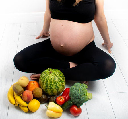 Pregnant woman with fruit and vegetables around her. Healthy eating concept. Pregnancy, slim skinny girl in black top and leggings isolated on white background. Diet and freshnessの写真素材