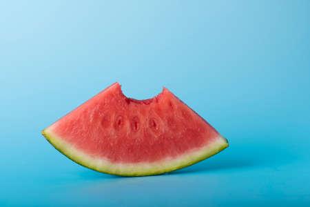 Watermelon slice on blue background with bite, refreshing fruitの写真素材