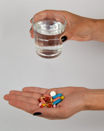 Woman holding in hands plenty of pills and a glass of waterの写真素材