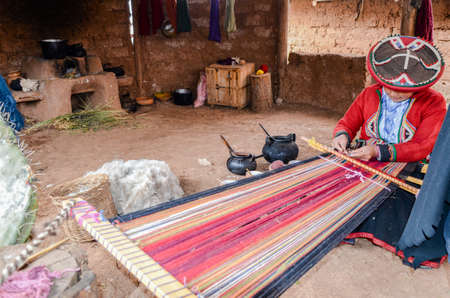 CHINCHERO, PERU- JUNE 3, 2013: Native Cusquena woman dressed in traditional colorful clothing works on a loom outside her houseのeditorial素材