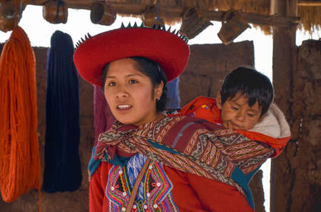 CHINCHERO, PERU- JUNE 3, 2013: Native Cusquena woman dressed in traditional colorful clothing explaining the dyeing threads and weaving process with her baby on her backのeditorial素材