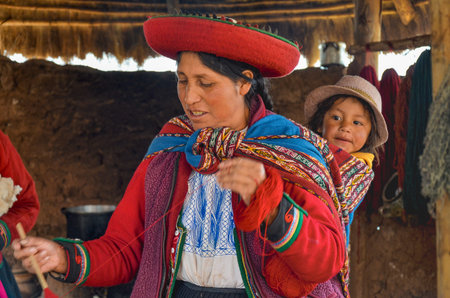 CHINCHERO, PERU- JUNE 3, 2013: Native Cusquena woman dressed in traditional colorful clothing explaining the dyeing threads and weaving process with her baby on her backのeditorial素材