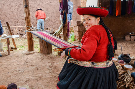 CHINCHERO, PERU- JUNE 3, 2013: Native Cusquena woman dressed in traditional colorful clothing works on a loom outside her houseのeditorial素材