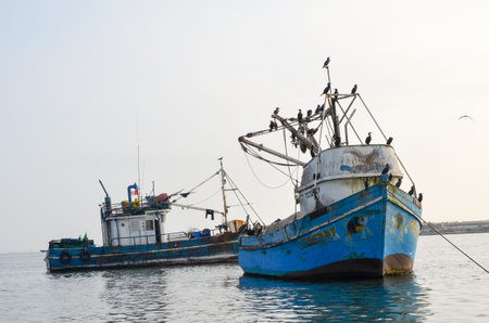 PARACAS, PERU- 11 JUNE, 2013: Old local fishing boats with fishing nets and seagulls anchored in the...