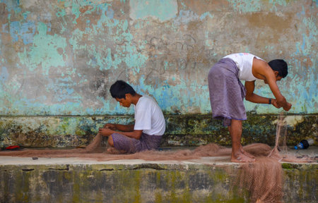 NGAPALI, MYANMAR- SEPTEMBER 27, 2016: Fishermen preparing their fishing nets in front of their house