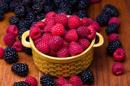 Bunch of raspberries in yellow ceramic bowl on a dark brown wood background.