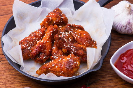 Chicken wings on cast iron pan with spices and sauce on wooden backgroundの写真素材