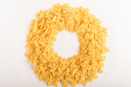 Heap of dried Farfalle Rigate Italian pasta ready to be cooked, isolated on a white table, top view or flat lay of healthy food displayed as a circleの写真素材