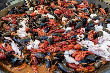 Mixed seafood cooked in a large traditional black fry pan at a street food festival, ready to eat seafood, side view, calamari, crabs, mussels with sauceの写真素材