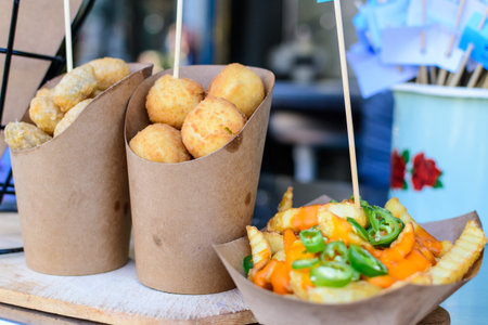 Group of Sicilian arancini in a brown paper cones and French fried potatoes with cheese cream and ...