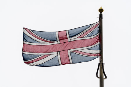 Flag of United Kingdom (the Union Jack also known as Union flag) blowing in the wind towards cloudy...