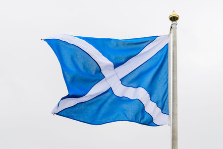 Flag of Scotland (Saltire or the Saint Andrew's Cross) blowing in the wind towards cloudy grey sky...