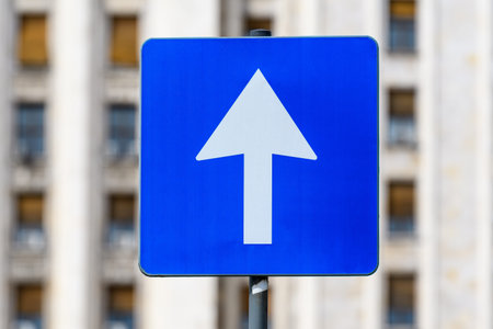 Road sign for single circulation direction, white arrow on blue panel towards clear blue sky