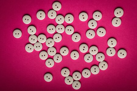 Large group of delicate light white wooden buttons on pink magenta textured cardboard  background, displayed centred, top view with space for text around, flat lay with laser cut wooden objectsの写真素材