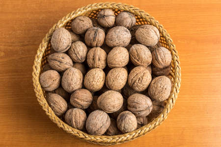 Walnuts in a wooden round bowl on a wooden table in soft focus, top view or flat lay of healthy vegan food, brown monochrome photoの写真素材