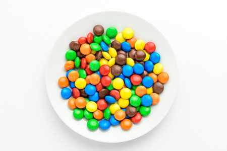 Group of small red, yellow, green, blue, brown and orange coated chocolate candies in a white round...