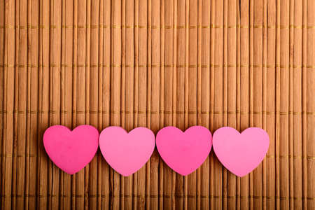 Four pink hearts on a brown bamboo table decoration, top view with space for text above, selective focusの写真素材