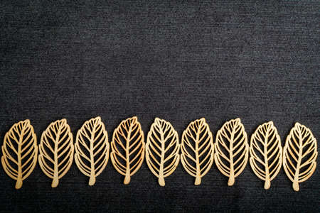 Line with nine delicate light brown wooden leaves on dark grey textile material background, top view with space for text on the right side, flat lay with laser cut wooden objectsの写真素材