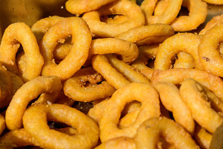 Large group of freshly fried calamari and onion rings on display for sale at a street food festival,...