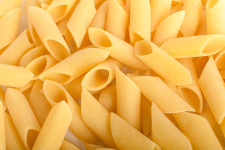 Heap of dried mezze penne rigate Italian pasta ready to be cooked, isolated on a white table, top view or flat lay of healthy foodの写真素材