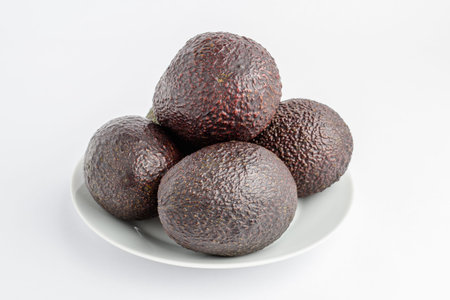 Four ripe ready to eat avocado fruits on a white plate on a white table, with side view