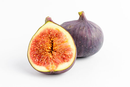 Fresh ripe organic figs on a white table, one whole fig and one sectioned in half, close up with...