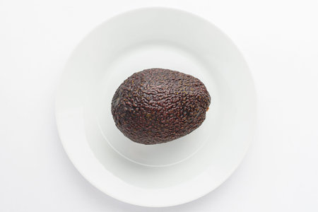 One ripe ready to eat avocado fruit on a white plate on a white table, top view