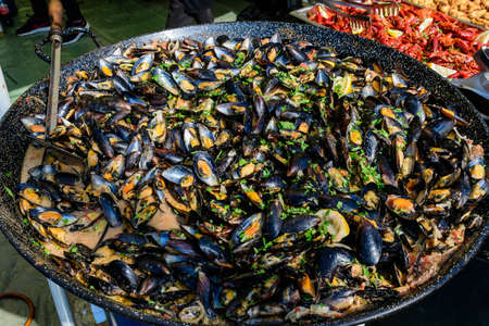 Large group of cooked black mussels with tomato and cream sauce at a street food festival, ready to eat seafood,  beautiful monochrome outdoor backgroundの写真素材