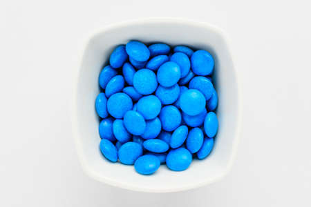 One squared white bowl with small blue colored chocolate coated candies, isolated on white background, top view or flat lay photoの写真素材