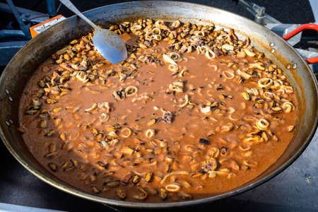 Close up of large portion of calamari rings cooked with tomato sauce in a black pan at a street food festival, displayed for sale, ready to eat healthy seafoodの写真素材