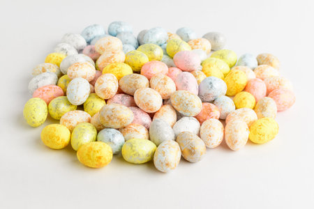 Heap of mixed chocolate coated Easter eggs candies isolated on a white table, tasty sugary dessert...