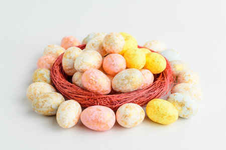 Mixed chocolate coated Easter eggs candies in a small red basket isolated on a white table, tasty...