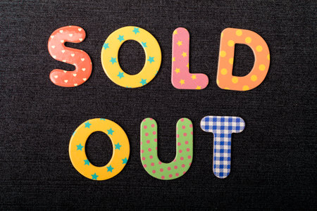 Card with Sold Out words made from mixed vivid colored wooden letters on a textured dark black textile material that can be used as a messageの写真素材