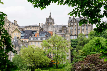Row of old historic buildings behind large green trees in Edinburgh, Scotland in a cloudy rainy summer dayの写真素材