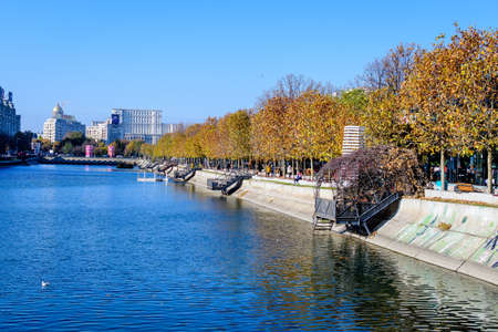 Bucharest, Romania, 22 November 2020: Landscape with Dambovita river, old buildings and yellow, orange and brown leaves in large trees in the center of Bucharest, Romania, in a sunny autumn dayのeditorial素材