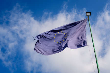 European Union flag blowing in the wind towards cloudy blue sky in a sunny sprng dayの写真素材